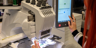 Eine weibliche Person erstellt an einer Stickmaschine im Hylec einen Auftrag zur Programmierung.